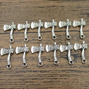Pode incluir: Um conjunto de 12 pingentes de machado prateados. Cada pingente apresenta um design de machado detalhado com uma superfície texturizada. Os pingentes são perfeitos para adicionar um toque rústico a joias ou artesanato.