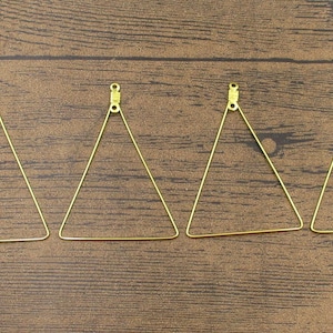 May include: Four gold triangle-shaped earring hoops with a jump ring at the top.