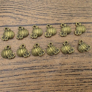 Könnte beinhalten: Ein Set mit 14 antiken goldenen Kürbis-Anhängern. Die Anhänger sind mit einer Kürbisform und Blättern verziert.