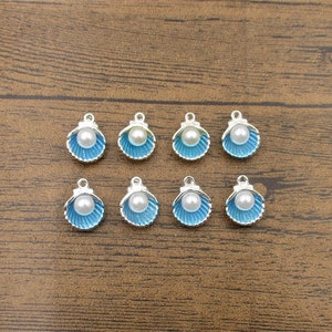 May include: Eight silver charm pendants shaped like seashells with a blue enamel finish and a white pearl in the center.
