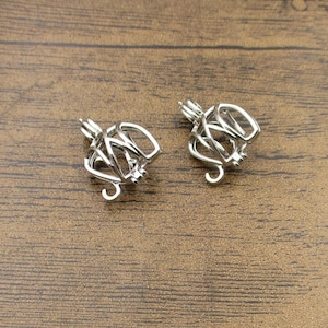 May include: Two silver charm cages with intricate designs. The cages are open and appear to be made of multiple layers of metal.