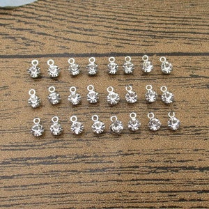 Puede incluir: Una colección de 24 abalorios de metal plateados con detalles de cristal transparente. Cada abalorio tiene un pequeño bucle para sujetarlo a joyas u otras manualidades.