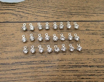 May include: A collection of 24 silver-toned metal charms with clear rhinestone accents. Each charm features a small loop for attaching to jewelry or other crafts.