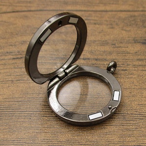 May include: A silver-toned locket with a hinged lid and a clear glass insert. The locket has a small loop at the top for attaching a chain.