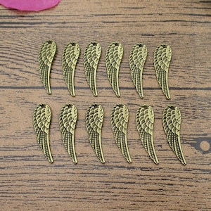 May include: A set of 14 gold-toned metal angel wing charms. The wings are detailed and have a vintage look.