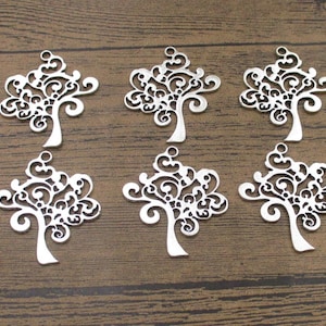 May include: Six silver metal tree charms with intricate filigree designs. The charms are arranged in two rows of three on a wooden surface.