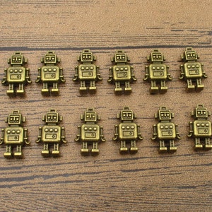 May include: Twelve antique gold robot charms, each with a detailed design, arranged in two rows on a wooden surface.
