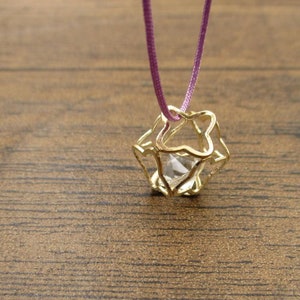 May include: A gold cage pendant necklace with a clear crystal inside. The necklace is on a purple cord.