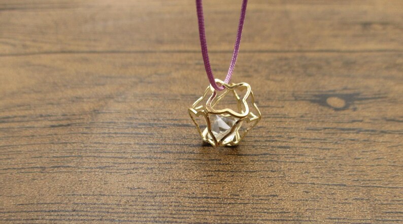 May include: A gold cage pendant necklace with a clear crystal inside. The necklace is on a purple cord.
