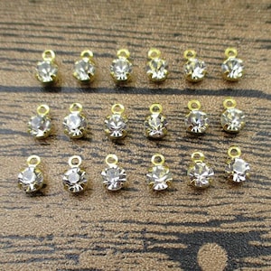 Puede incluir: Veinte abalorios de metal dorado con diamantes de imitación transparentes. Cada abalorio tiene un pequeño bucle para sujetarlo a joyas u otras manualidades.