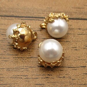 Puede incluir: Tres botones de perla blanca con adornos de metal dorado. Los botones tienen un dise&ntilde;o decorativo con un motivo floral.