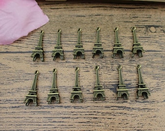 May include: A set of 12 bronze-colored Eiffel Tower charms. The charms are about 2 cm tall and have a loop at the top for attaching to jewelry or other crafts.
