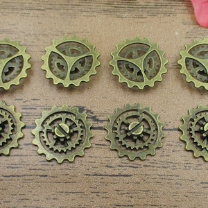 Puede incluir: Ocho engranajes de metal de color dorado antiguo con diseños intrincados. Los engranajes están dispuestos en dos filas de cuatro, con la fila superior ligeramente desplazada de la fila inferior.