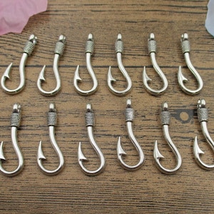 May include: A set of 15 silver-toned metal fish hook charms. The hooks are all the same size and shape, and they have a slightly textured finish.