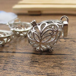 May include: Silver filigree charm with a delicate floral design. The charm is open on one side and has a loop for attaching to a necklace or bracelet.