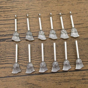 May include: A set of 16 silver-toned metal charms shaped like broomsticks. The charms are ideal for adding a touch of whimsy to jewellery or crafts.