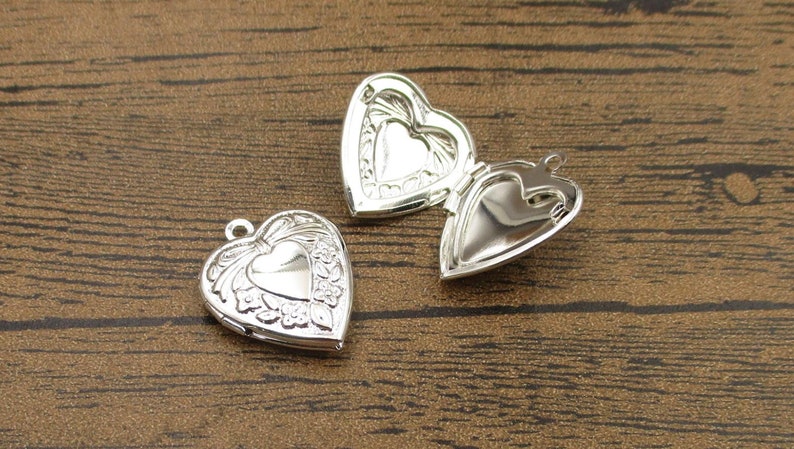 May include: Two silver heart-shaped locket pendants with intricate floral designs. The lockets are open, revealing the empty interior.
