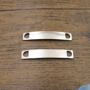 Puede incluir: Dos etiquetas en blanco de metal plateado con bordes redondeados y agujeros para sujetar a un llavero u otro artículo.