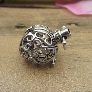 Peut inclure: Pendentif en forme de cœur en cage de filigrane argenté avec une ouverture à charnière. La cage est finement détaillée avec des motifs en spirale.