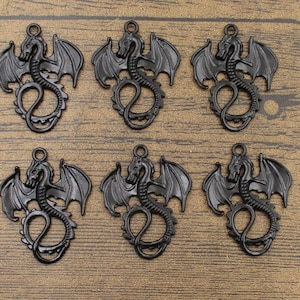 Könnte beinhalten: Sechs schwarze Metall-Drachen-Anhänger mit ausgebreiteten Flügeln. Die Anhänger sind detailliert und haben eine leicht gealterte Oberfläche.