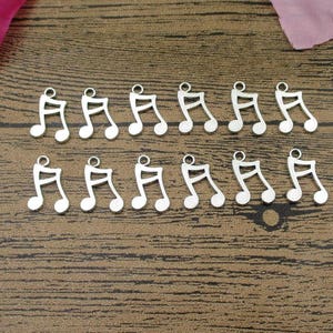 May include: A collection of 18 silver music note charms. The charms are all the same size and shape, and they are arranged in two rows on a wooden surface.