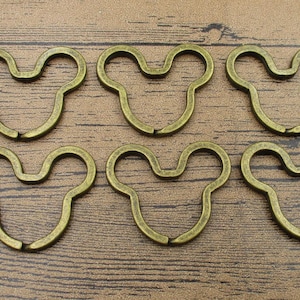 May include: Six gold-toned metal keychains shaped like a Mickey Mouse head. The keychains are all the same size and shape, and they are arranged in two rows of three.