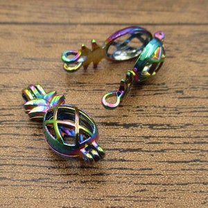 Könnte beinhalten: Nahaufnahme mehrerer schillernder Ananas-förmiger Anhänger. Die Anhänger sind aus Metall gefertigt und weisen ein hohles, käfigartiges Design auf. Die Ananas-Oberteile haben eine sternartige Form. Die Anhänger haben eine Schlaufe zum Befestigen an Schmuck oder anderen Bastelarbeiten.