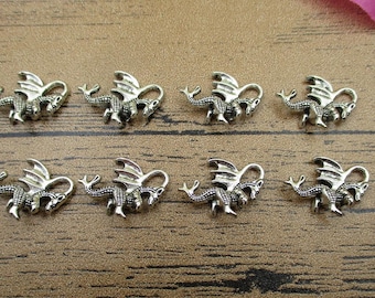May include: Eight silver dragon charms with detailed wings and tails. The charms are arranged in two rows of four on a wooden surface.