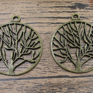 May include: Two antique bronze-colored metal tree of life charms with a circular shape and intricate cut-out designs. The charms have a loop at the top for hanging.