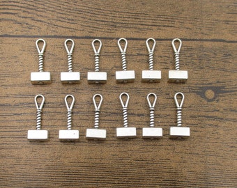 May include: A set of 15 silver-toned metal charms shaped like a hammer. The charms have a loop at the top for attaching to jewelry or other crafts.