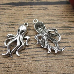 May include: Two silver octopus charm pendants. One octopus is facing forward with its tentacles outstretched, the other is facing backward with its tentacles curled.