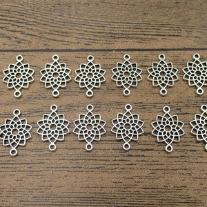 May include: Twelve silver-toned metal charms in the shape of a mandala with a decorative openwork design. Each charm has two loops for attaching to jewelry or other crafts.