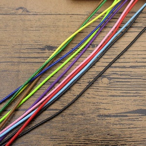May include: Assortment of colourful waxed cords in various colours, including black, red, blue, green, yellow, and pink. The cords are arranged in a fan shape on a wooden surface.