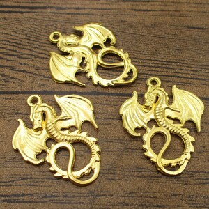 May include: Three gold-colored metal dragon charms with intricate details. Each charm features a dragon with wings outstretched and a curled tail.