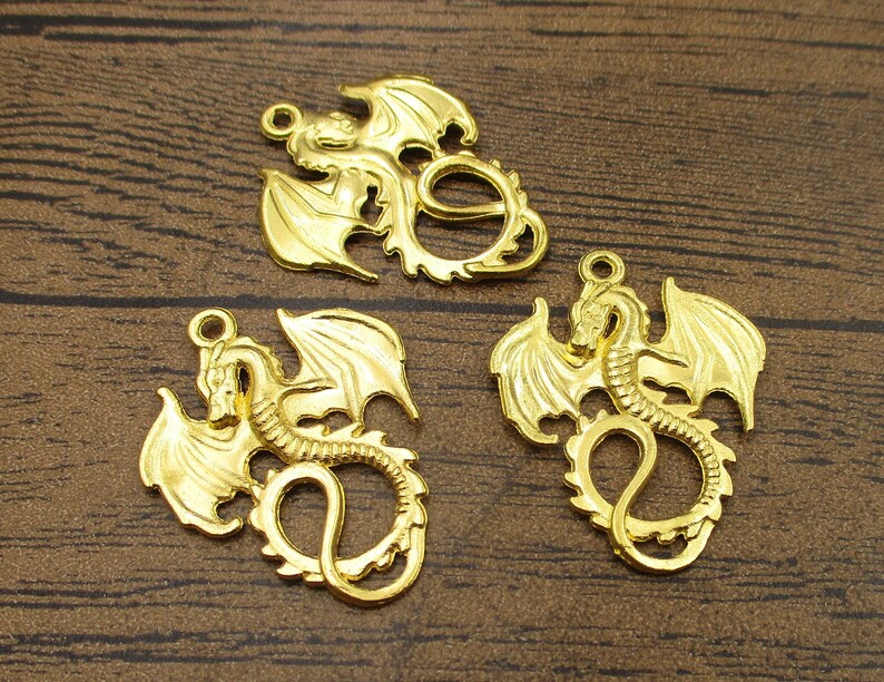 May include: Three gold-colored metal dragon charms with intricate details. Each charm features a dragon with wings outstretched and a curled tail.