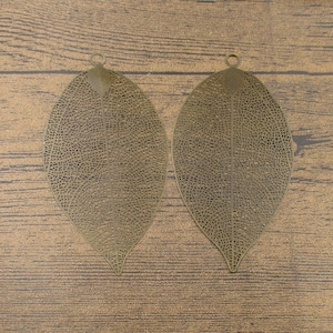 May include: Two antique gold leaf-shaped metal charms with intricate cut-out designs. The charms have a hole at the top for hanging.