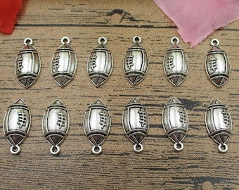May include: A set of 12 silver-toned metal charms shaped like footballs. The charms have a textured surface and a loop at the top for attaching to jewelry or other crafts.