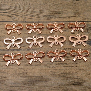 Puede incluir: Una colección de 15 abalorios de lazo de oro rosa. Los abalorios están hechos de metal y tienen un acabado brillante. Son perfectos para añadir un toque de elegancia a las joyas o las manualidades.