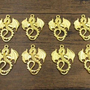 May include: Eight gold-colored metal dragon charms with wings outstretched. The charms are detailed and have a three-dimensional appearance.