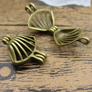 Op de afbeelding: Twee antieke goudkleurige metalen kooi-bedels met een decoratief waaiervormig ontwerp. De bedels zijn open en kunnen worden gebruikt voor het maken van sieraden of andere knutselwerkjes.