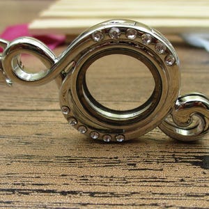 May include: A silver locket charm shaped like a treble clef with a clear glass insert and a row of clear rhinestones around the edge.