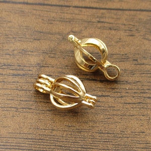 May include: Two gold-toned metal pearl cage pendants. The cages are open on one side and have a small loop on the other side for attaching to a chain or cord.