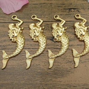 May include: Four gold-tone mermaid charms with a detailed design. Each charm features a mermaid with flowing hair and a tail.