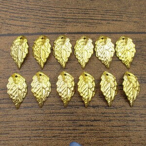 May include: A set of 12 gold-coloured metal leaf charms. The leaves are detailed and have a slightly textured surface.