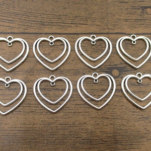 May include: Ten silver double heart-shaped metal charms with a loop at the top for hanging.