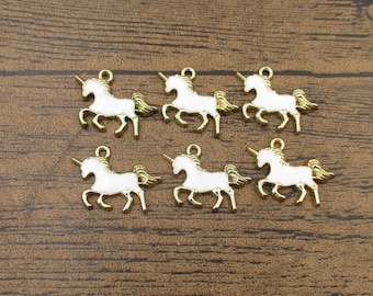 Op de afbeelding: Zes gouden metalen eenhoornbedels met wit emaille. De bedels zijn in de vorm van een rennende eenhoorn met een hoorn, manen en staart.