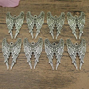 May include: Ten silver angel wing charms with a detailed design. The wings are about 2 inches long and have a hole at the top for attaching to jewelry or other crafts.