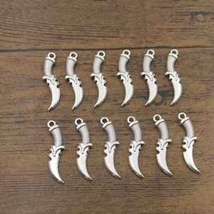 Puede incluir: Un conjunto de 14 abalorios de metal plateados en forma de dagas. Los abalorios tienen un diseño detallado y son perfectos para añadir un toque de estilo atrevido a los proyectos de joyería.