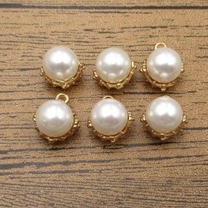 Puede incluir: Seis abalorios de perla blanca con engastes dorados. Las perlas son redondas y tienen un acabado liso y brillante. Los engastes dorados son ornamentados y tienen un dise&ntilde;o delicado.