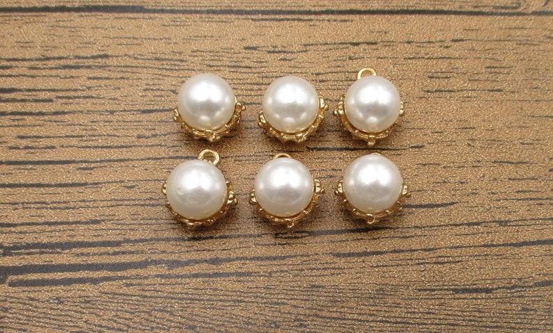 Puede incluir: Seis abalorios de perla blanca con engastes dorados. Las perlas son redondas y tienen un acabado liso y brillante. Los engastes dorados son ornamentados y tienen un dise&ntilde;o delicado.